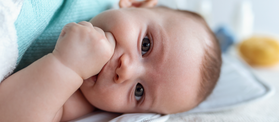 baby with hand on mouth lying in crib