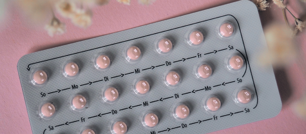 birth control pills on pink background with flower petals